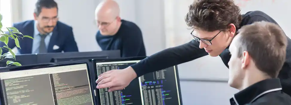 Szene mit Dozent und Schüler vor einem Computer am Arbeitsplatz